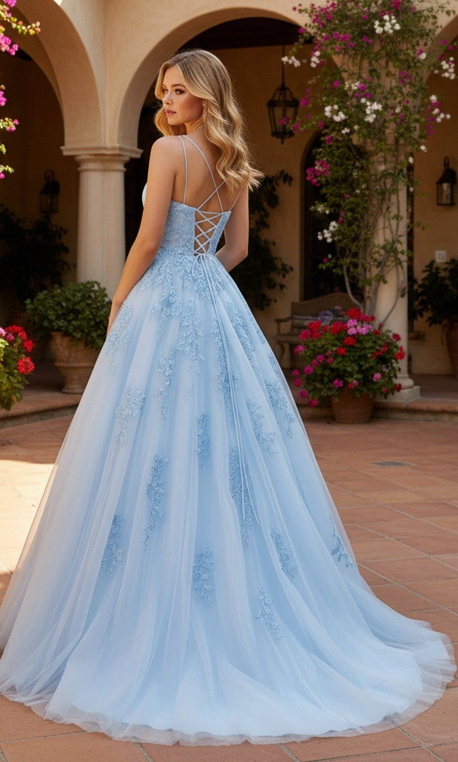 A woman stands outdoors on a tiled patio in the PromGirl Exclusive 250228 long prom dress—a light blue lace-embroidered gown with an adjustable lace-up back—surrounded by potted flowers and arched columns.